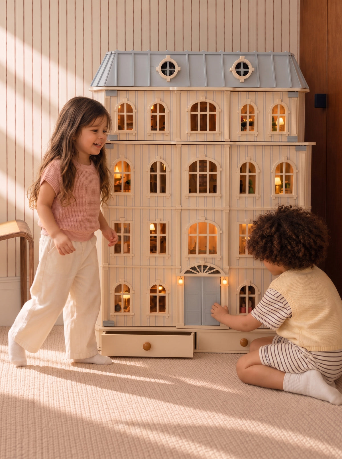 Smiling girl walking toward the illuminated House of Monaco dollhouse as a child opens its front door.