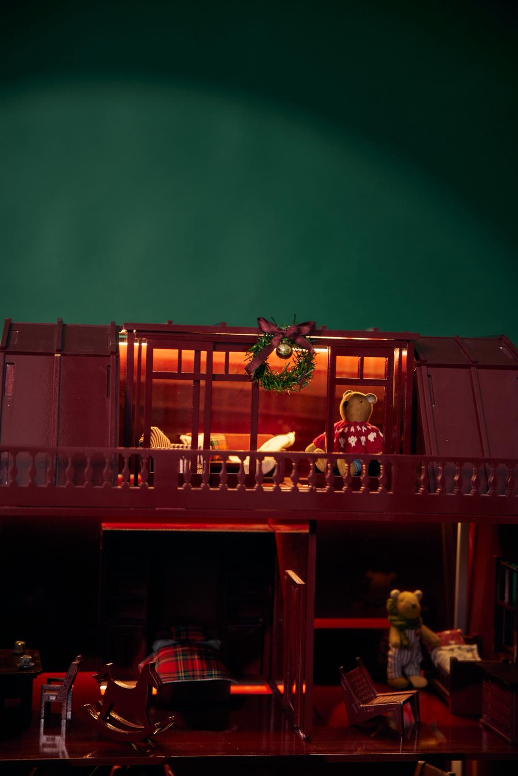 Red toy house with a wreath on top, surrounded by Christmas decorations