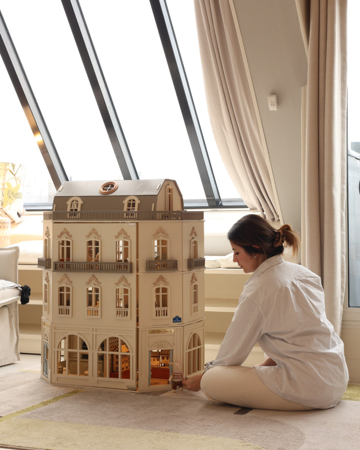 The House of Paris dollhouse is displayed in a home setting as miniature furniture is arranged inside one of its detailed rooms.
