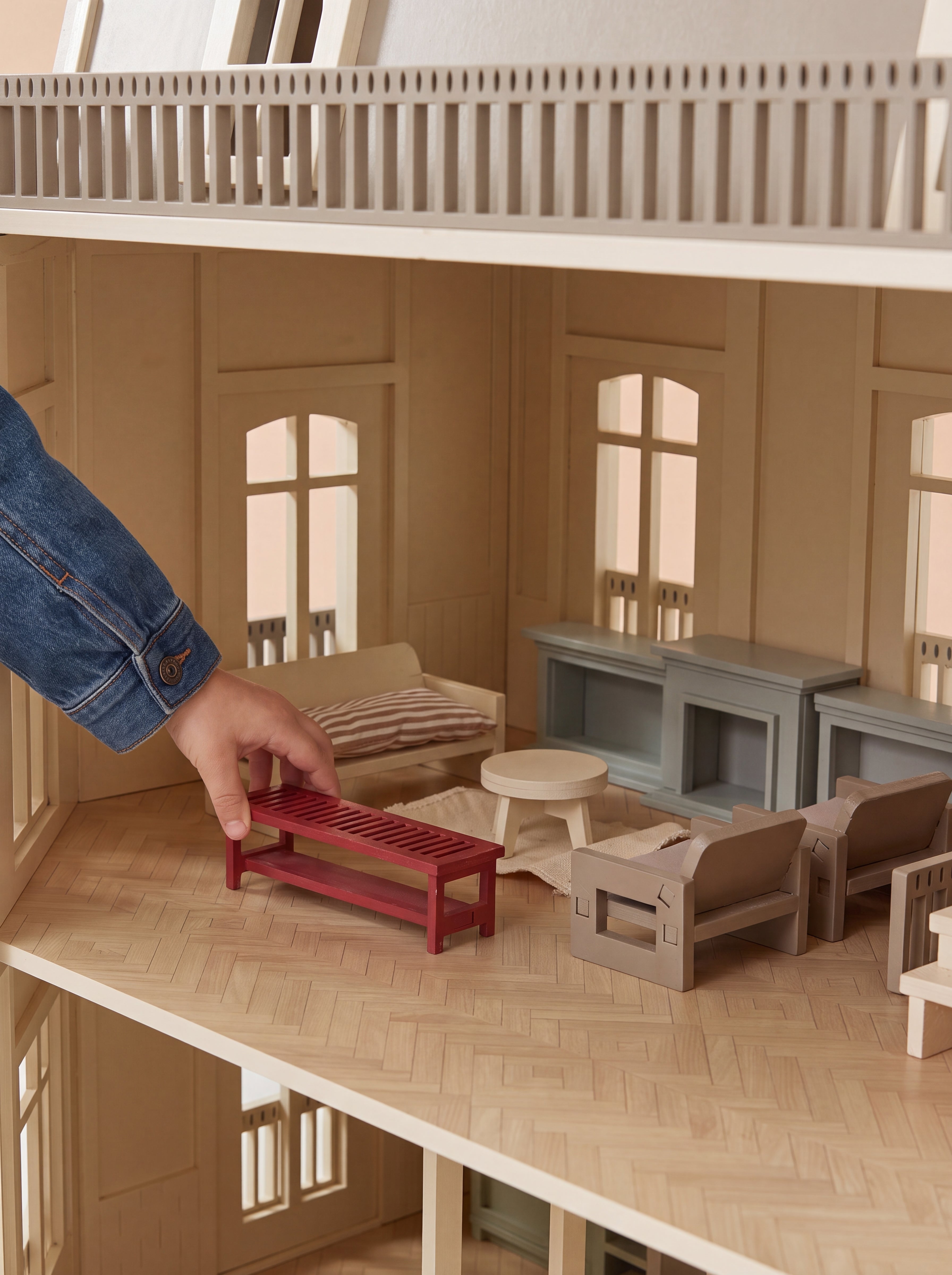 A hand places miniature furniture inside the open House of Paris dollhouse, highlighting the detailed living room interior.