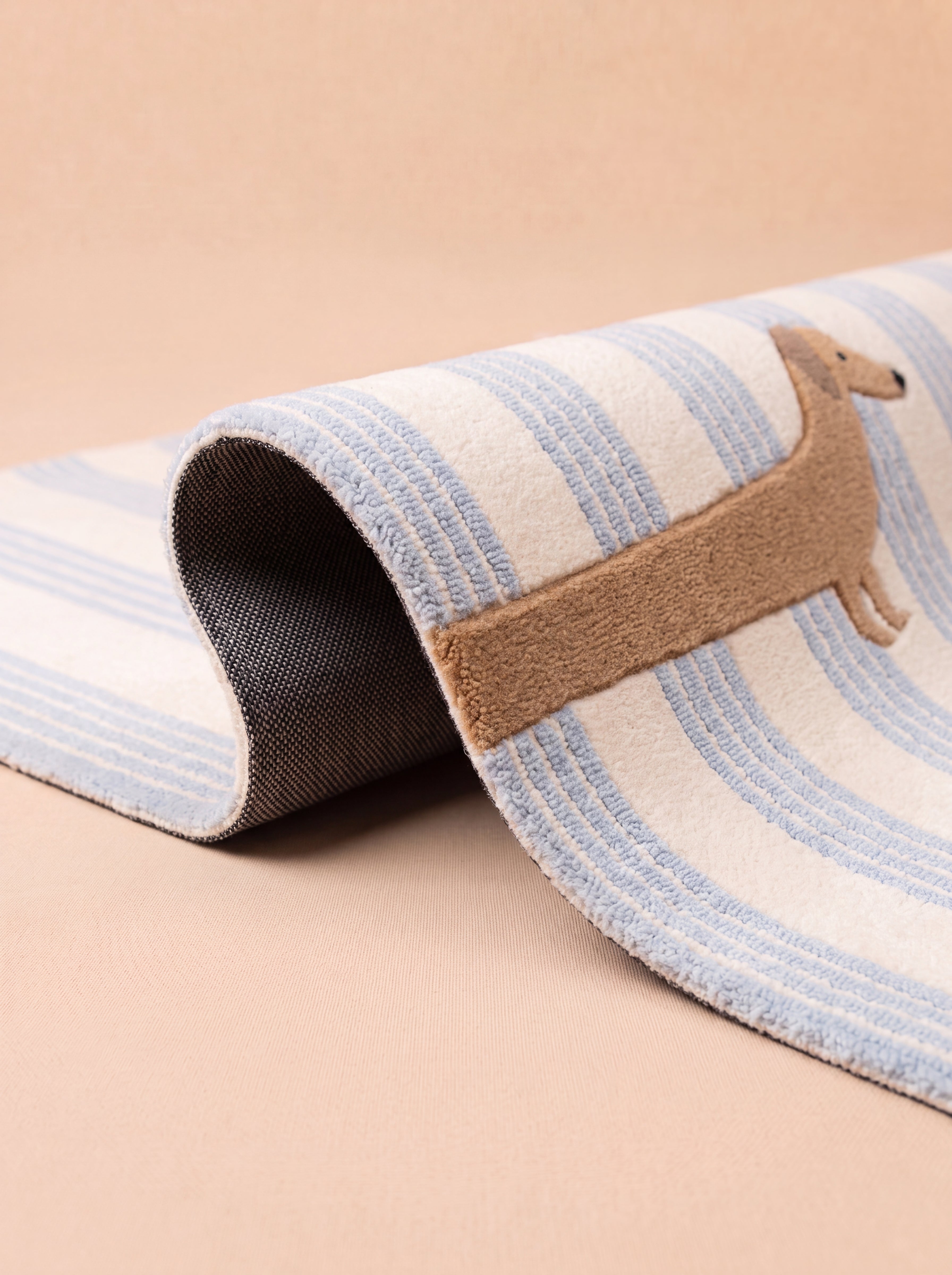 Folded blue striped rug with a woven dachshund design, highlighting the textured surface and non-slip backing.