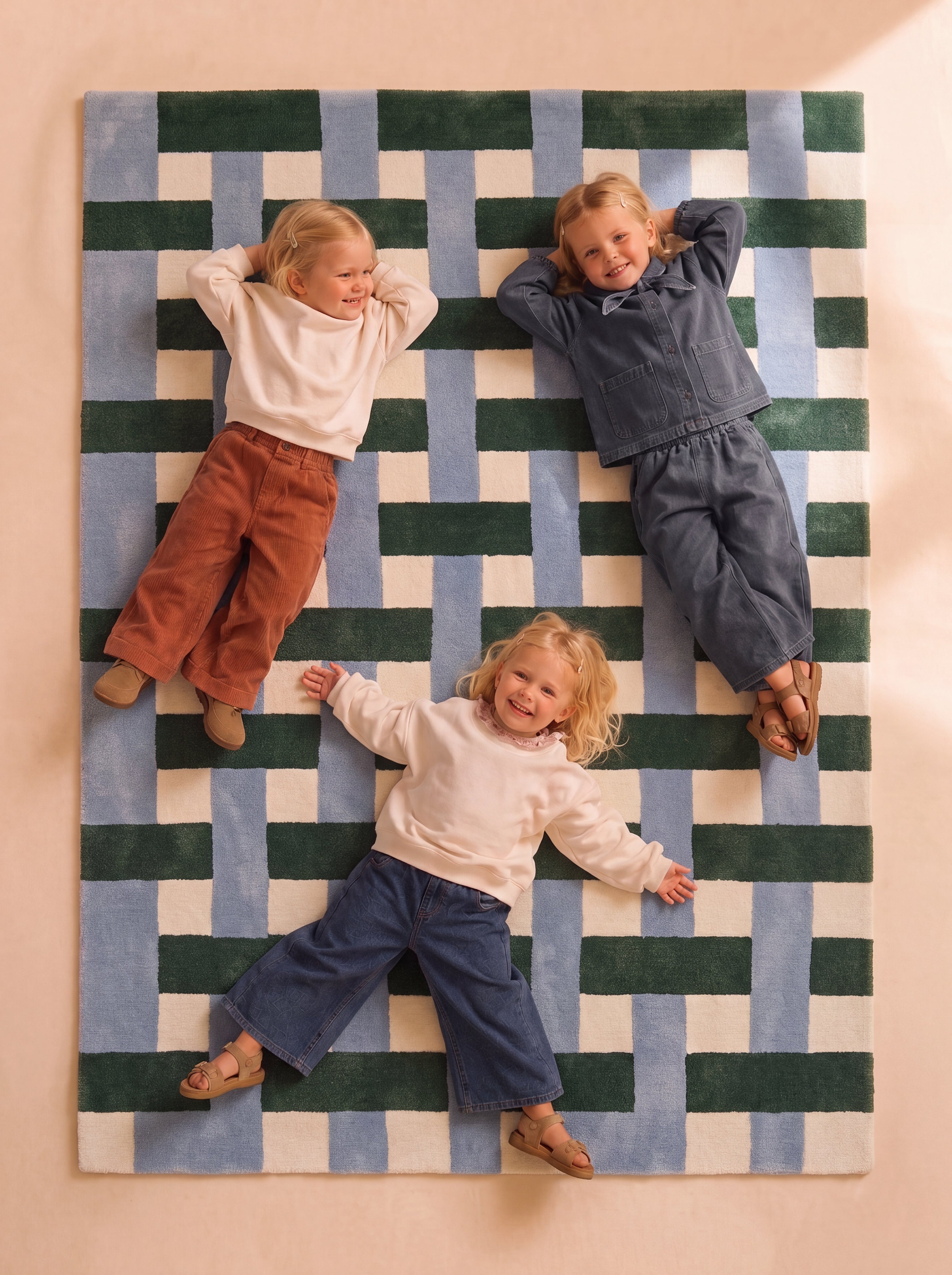 Three children sitting on a hand-tufted rug with a geometric pattern in blue, green, and cream.