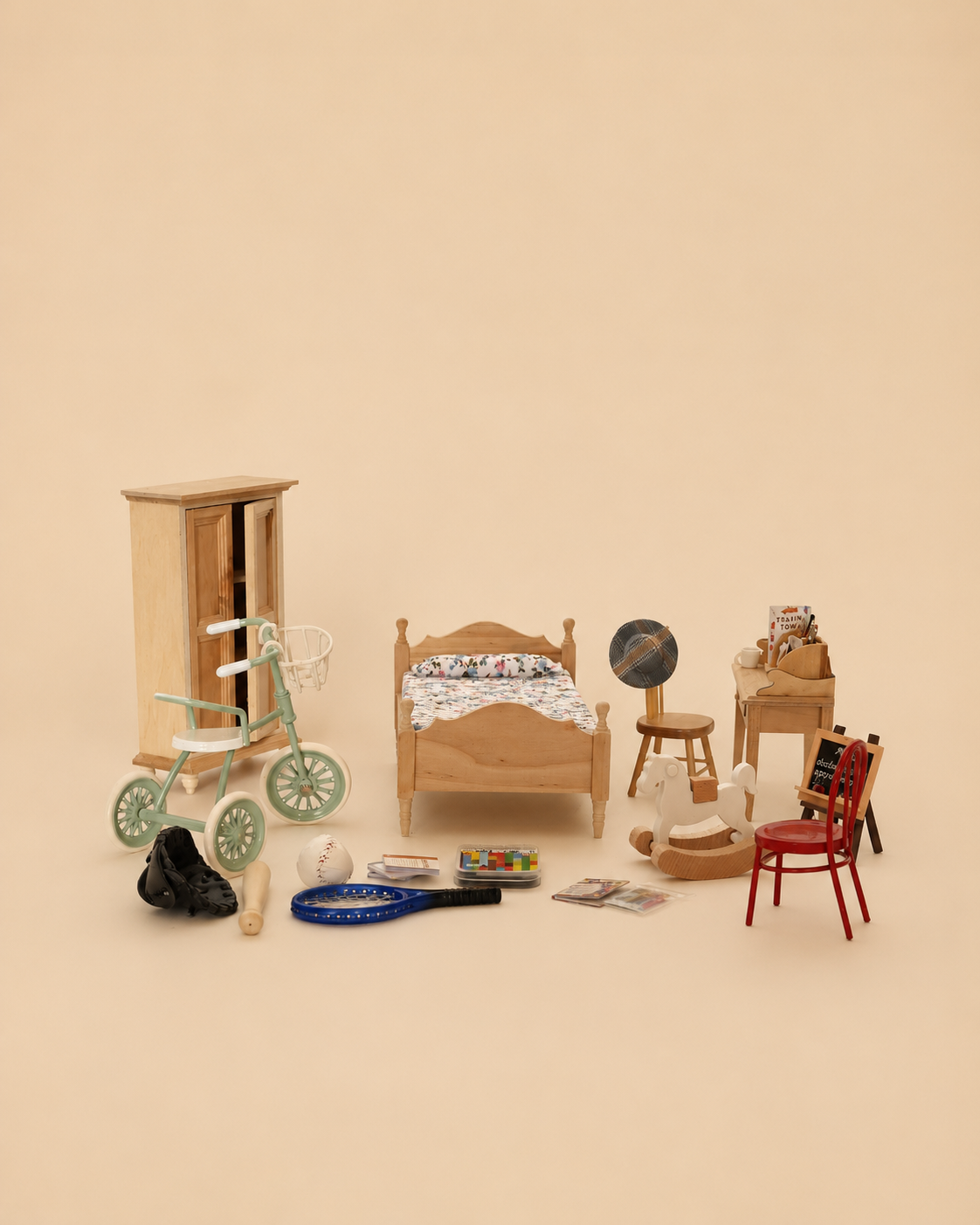 A miniature dollhouse-style bedroom furniture set arranged on a warm beige studio background. The set includes a light wood bed frame with floral bedding, a matching wooden wardrobe, a small red chair, a wooden stool, a desk with books, a tricycle in mint green, a black toy car, and several small accessories.