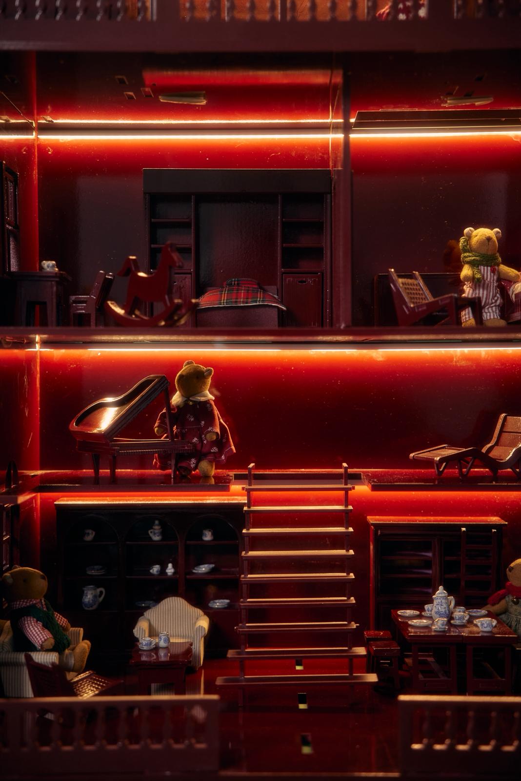 christmas dollhouse with teddy bears and furniture, illuminated by red lights.