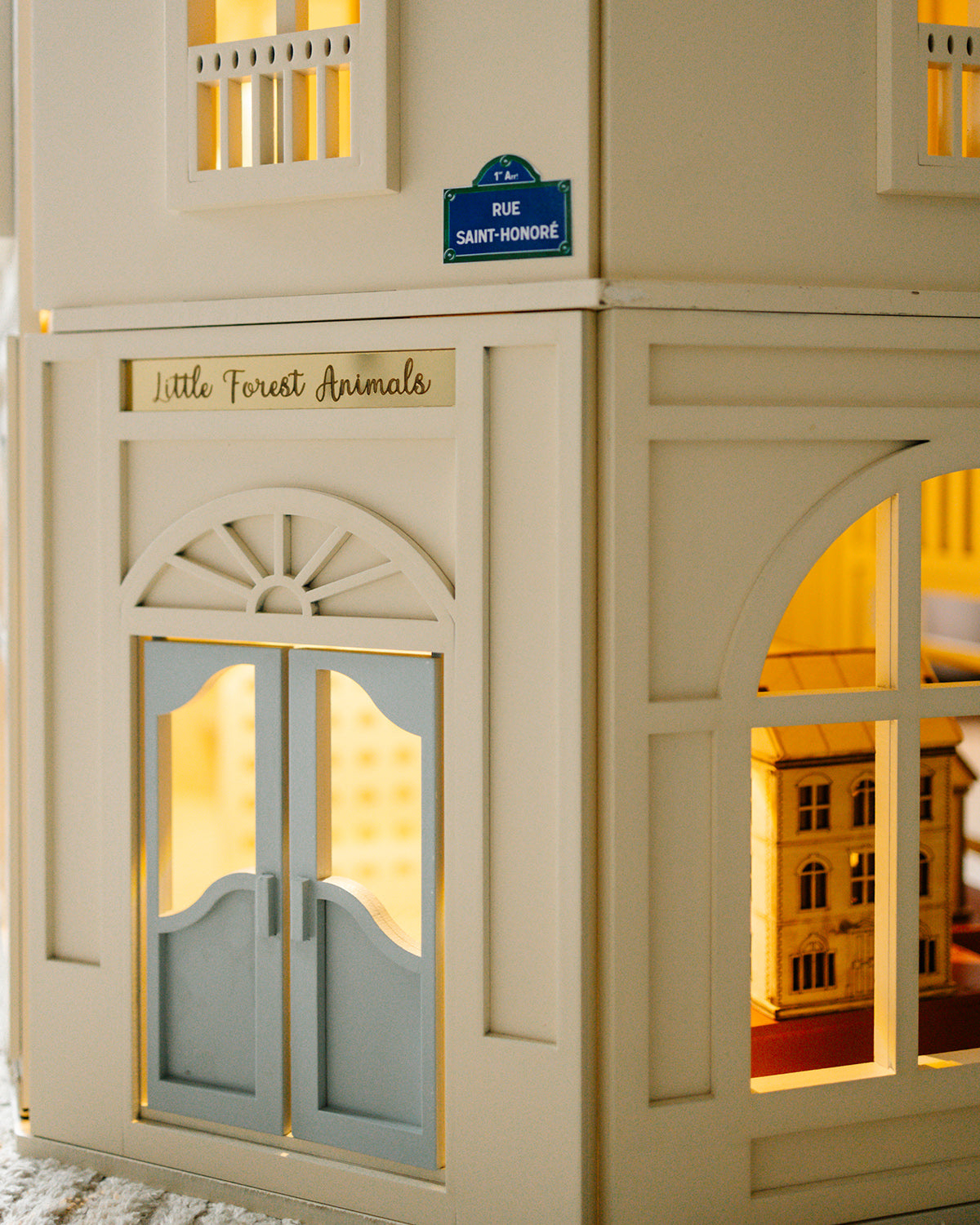 A closer look at the front entrance of the House of Paris dollhouse, featuring classic architectural details and warm interior lighting.