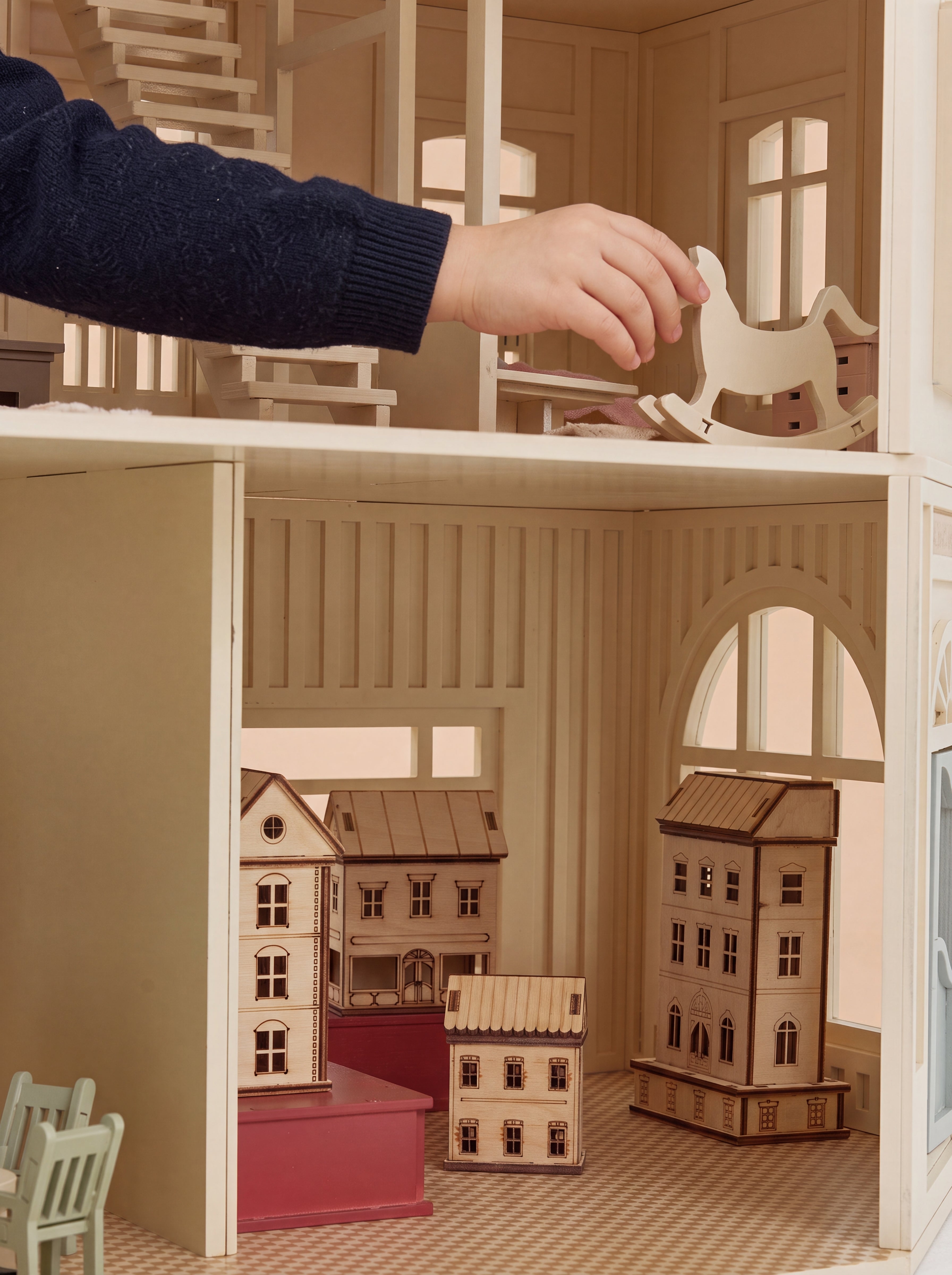 A wooden rocking horse is placed inside the House of Paris dollhouse, revealing the detailed playroom and miniature houses below.