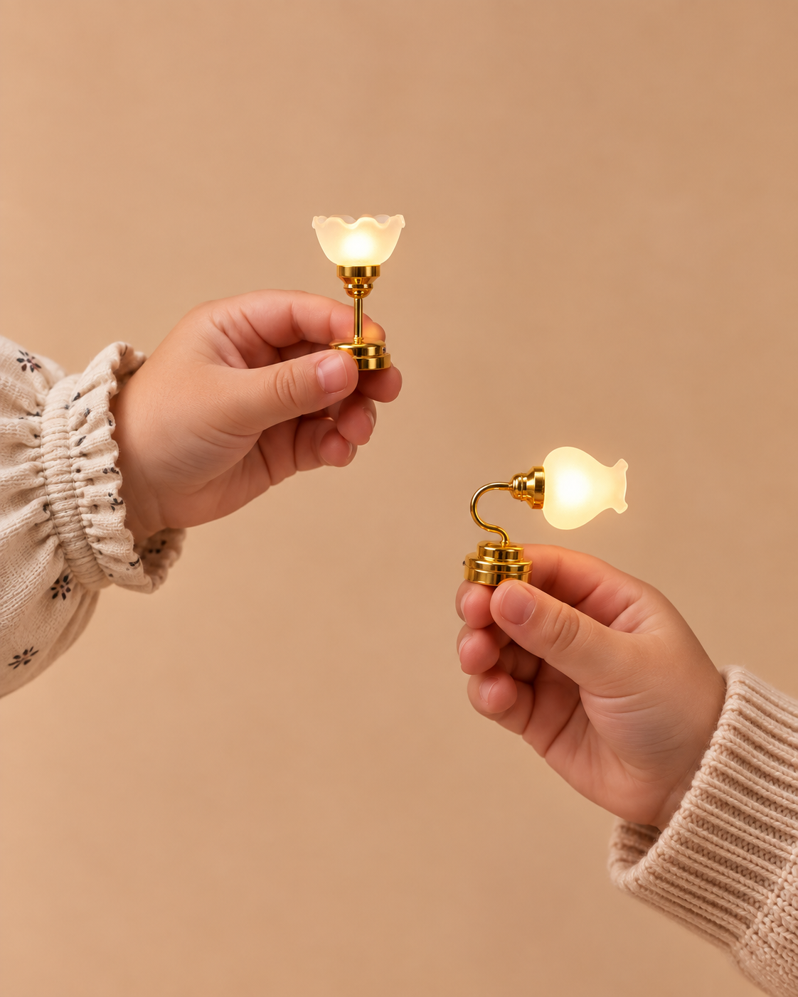 Two hands holding miniature gold-toned fairy lights with glowing frosted bell-shaped shades against a solid beige background.