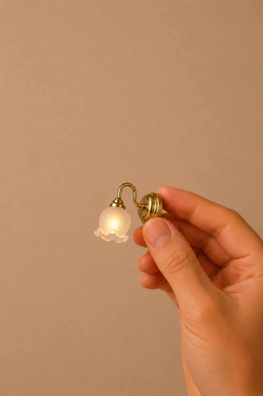 Miniature brass wall lamp with a glowing white glass shade held in a hand.