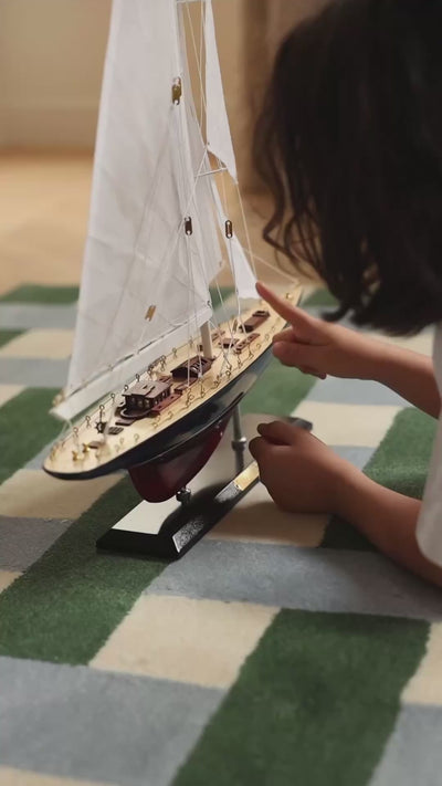 Child exploring the details of a handcrafted wooden sailboat model with a finger on the deck.
