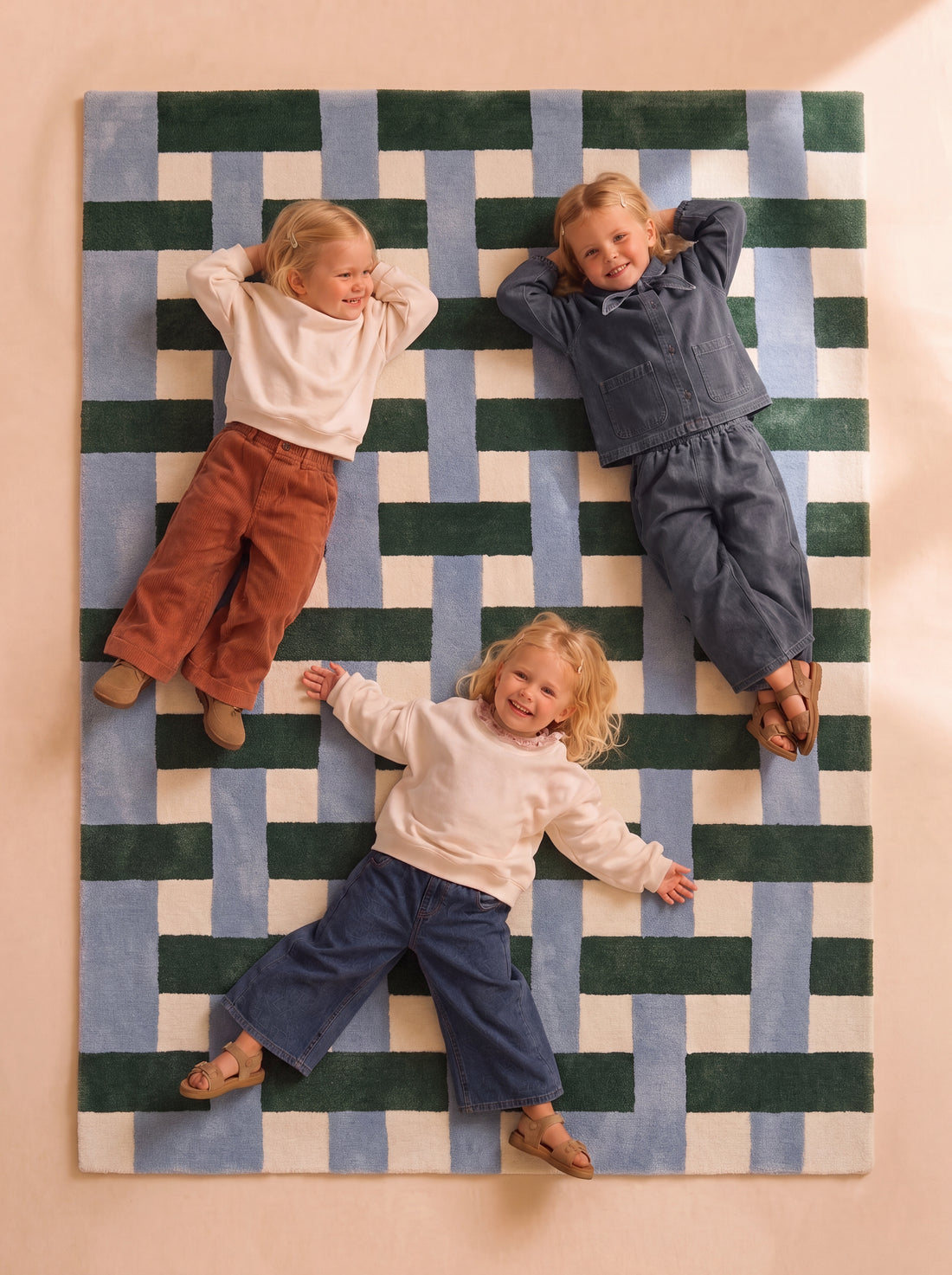 Three children sitting on a hand-tufted rug with a geometric pattern in blue, green, and cream.