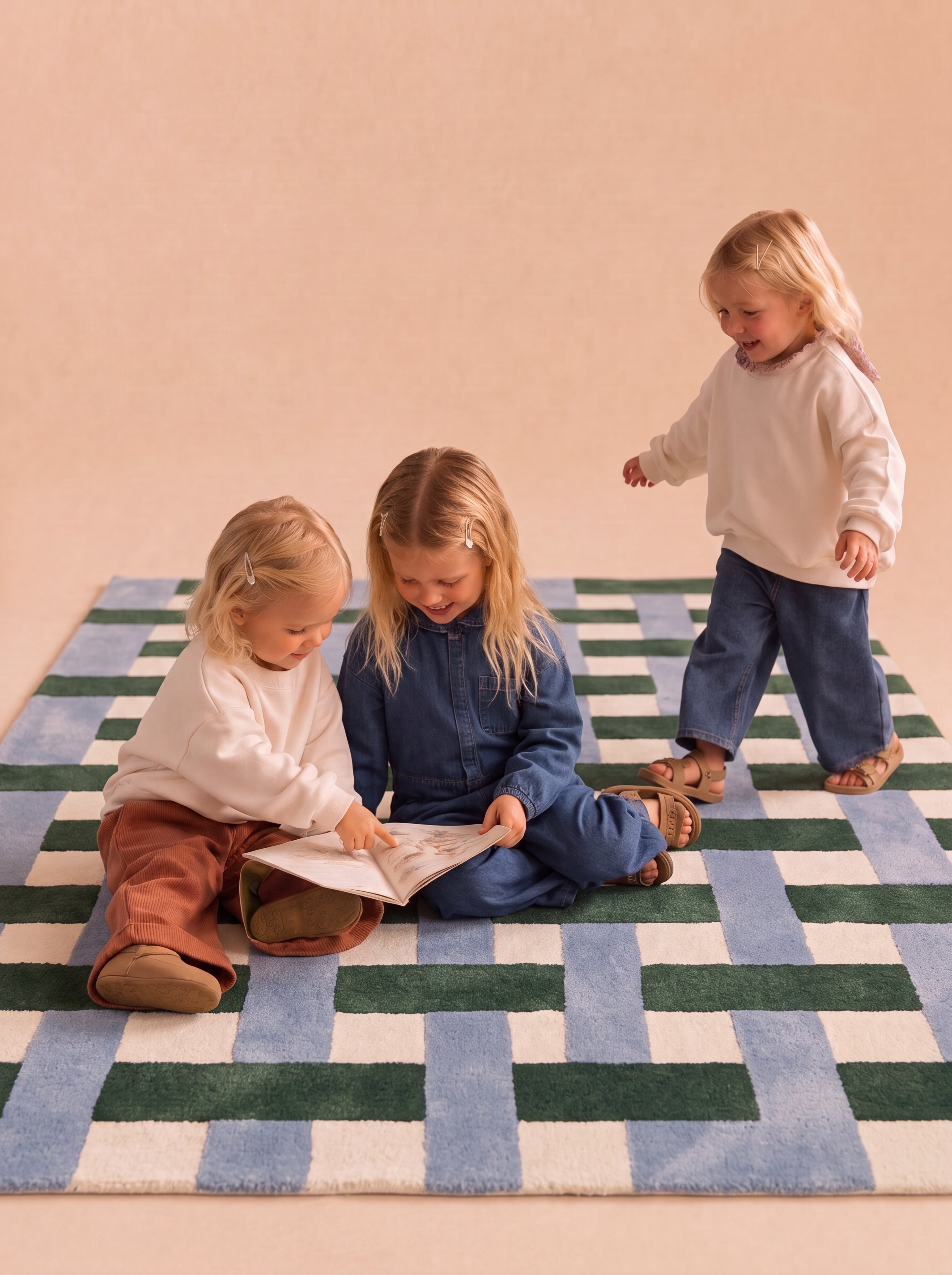 Three children reading a book while sitting on a hand-tufted rug with a blue, green, and cream geometric pattern.