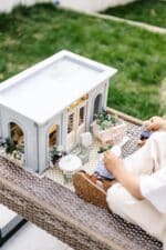 Miniature wooden flower shop dollhouse in pastel blue, with plants, a bunny figure, and charming outdoor details.