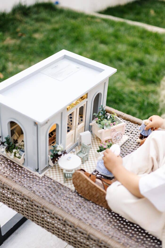 Miniature wooden flower shop dollhouse in pastel blue, with plants, a bunny figure, and charming outdoor details.