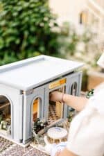 Miniature wooden flower shop dollhouse in pastel blue, with plants, a bunny figure, and charming outdoor details
