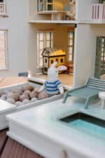 Handcrafted wooden dollhouse with miniature furniture and details, displayed in a minimal setting.