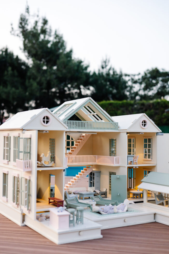 Handcrafted wooden dollhouse with miniature furniture and details, displayed in a minimal setting.