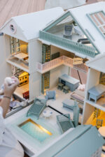 Handcrafted wooden dollhouse with miniature furniture and details, displayed in a minimal setting.
