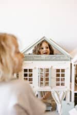 Handcrafted wooden dollhouse with miniature furniture and details, displayed in a minimal setting.