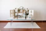 Handcrafted wooden dollhouse with miniature furniture and details, displayed in a minimal setting.