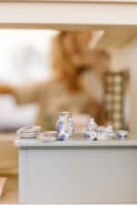 Handcrafted wooden dollhouse with miniature furniture and details, displayed in a minimal setting.