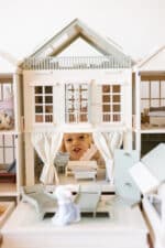Handcrafted wooden dollhouse with miniature furniture and details, displayed in a minimal setting.