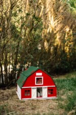 Handcrafted red wooden barn-style dollhouse with green roof, designed by Little Forest Animals for sustainable and imaginative play.