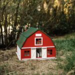 Handcrafted red wooden barn-style dollhouse with green roof, designed by Little Forest Animals for sustainable and imaginative play.
