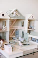 Handcrafted wooden dollhouse with miniature furniture and details, displayed in a minimal setting.