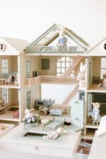 Handcrafted wooden dollhouse with miniature furniture and details, displayed in a minimal setting.