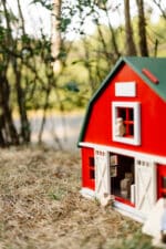Handcrafted red wooden barn-style dollhouse with green roof, designed by Little Forest Animals for sustainable and imaginative play.