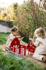 Handcrafted red wooden barn-style dollhouse with green roof, designed by Little Forest Animals for sustainable and imaginative play.