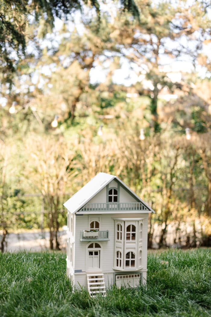 Victorian-style handcrafted white wooden dollhouse by Little Forest Animals, photographed outdoors on green grass in natural light.
