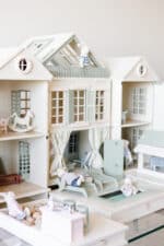 Handcrafted wooden dollhouse with miniature furniture and details, displayed in a minimal setting.