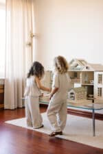 Handcrafted wooden dollhouse with miniature furniture and details, displayed in a minimal setting.