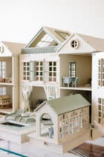 Handcrafted wooden dollhouse with miniature furniture and details, displayed in a minimal setting.