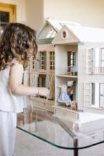 Handcrafted wooden dollhouse with miniature furniture and details, displayed in a minimal setting.