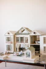 Handcrafted wooden dollhouse with miniature furniture and details, displayed in a minimal setting.