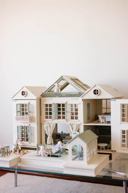 Handcrafted wooden dollhouse with miniature furniture and details, displayed in a minimal setting.
