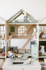 Handcrafted wooden dollhouse with miniature furniture and details, displayed in a minimal setting.
