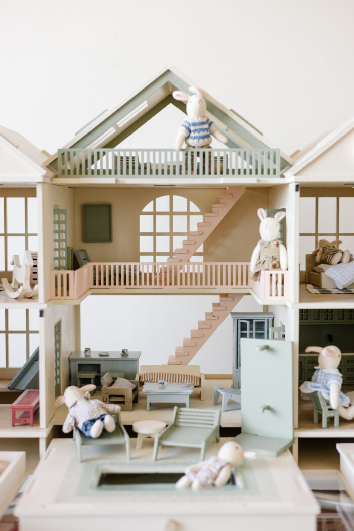 Handcrafted wooden dollhouse with miniature furniture and details, displayed in a minimal setting.