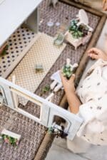 Miniature wooden flower shop dollhouse in pastel blue, with plants, a bunny figure, and charming outdoor details.